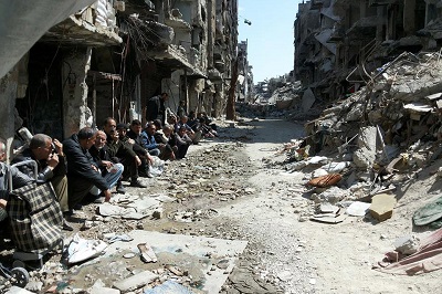 Na zdjęciu: Palestyńczycy siedzą w ruinach obozu uchodźców Jarmouk w Syrii dostały się (Źródło: UNRWA)