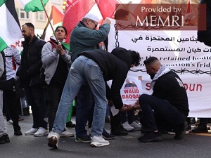 Na powyszym zdjciu wida grup protestujcych podnoszcych flagi Palestyny i Samidoun. Dwóch modych mczyzn, z których jeden ma na sobie sweter z kolaem portretów uzbrojonych palestyskich terrorystów, przyczepia do banera plakat ze zdjciem palestyskiego winia Walida Dakkaha. Dakkah zosta skazany w 1986 roku za udzia w porwaniu i zabójstwie izraelskiego onierza Mosze Tamama w 1984 roku. Na sztandarze widnieje tekst, zarówno po arabsku, jak i po angielsku, który brzmi: „Uwolni zatrzymane ciaa z chodni okupanta” [2]