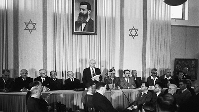 Izraelski ojciec-założyciel i pierwszy premier, David Ben-Gurion, deklaruje niepodległość pod dużym portretem Theodora Herzla, założyciela nowoczesnego syjonizmu. Zdjęcie: Wikimedia Commons.
