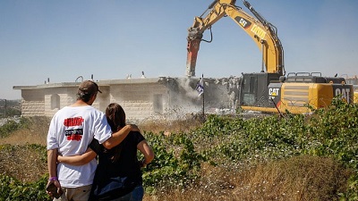 Maestwo Izraelczyków patrzy na dwig, który burzy dom w nielegalnej ydowskiej dzielnicy Netiv Ha’avot w Gusz Ecjon, dwa dni po eksmisji mieszkaców, 14 czerwca 2018. Zdjcie: Gershon Elinson/Flash90.
