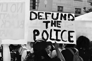 Demonstrant na proteście w sprawie George'a Floyda trzyma znak „Defund the Police”, 5 czerwca 2020 r. Źródło: Taymaz Valley via Wikimedia Commons.