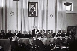 Założyciel Izraela i pierwszy premier David Ben-Gurion ogłasza niepodległość 14 maja 1948 r. pod dużym portretem Theodora Herzla, założyciela nowoczesnego syjonizmu, w Muzeum Tel Awiwu, obecnie Sala Niepodległości. Zdjęcie: Zoltan Kluger/GPO.