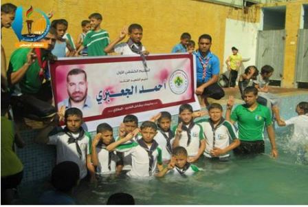 Dzieci w basenie przed portretem byego szefa militarnego skrzyda Hamasu, Ahmeda Al-Dabariego (Facebook.com/Gazacamps2014, 19 czerwca 2014)