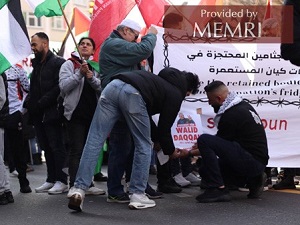 Na powyższym zdjęciu widać grupę protestujących podnoszących flagi Palestyny i Samidoun. Dwóch młodych mężczyzn, z których jeden ma na sobie sweter z kolażem portretów uzbrojonych palestyńskich terrorystów, przyczepia do banera plakat ze zdjęciem palestyńskiego więźnia Walida Dakkaha. Dakkah został skazany w 1986 roku za udział w porwaniu i zabójstwie izraelskiego żołnierza Mosze Tamama w 1984 roku. Na sztandarze widnieje tekst, zarówno po arabsku, jak i po angielsku, który brzmi: „Uwolnić zatrzymane ciała z chłodni okupanta” [2]